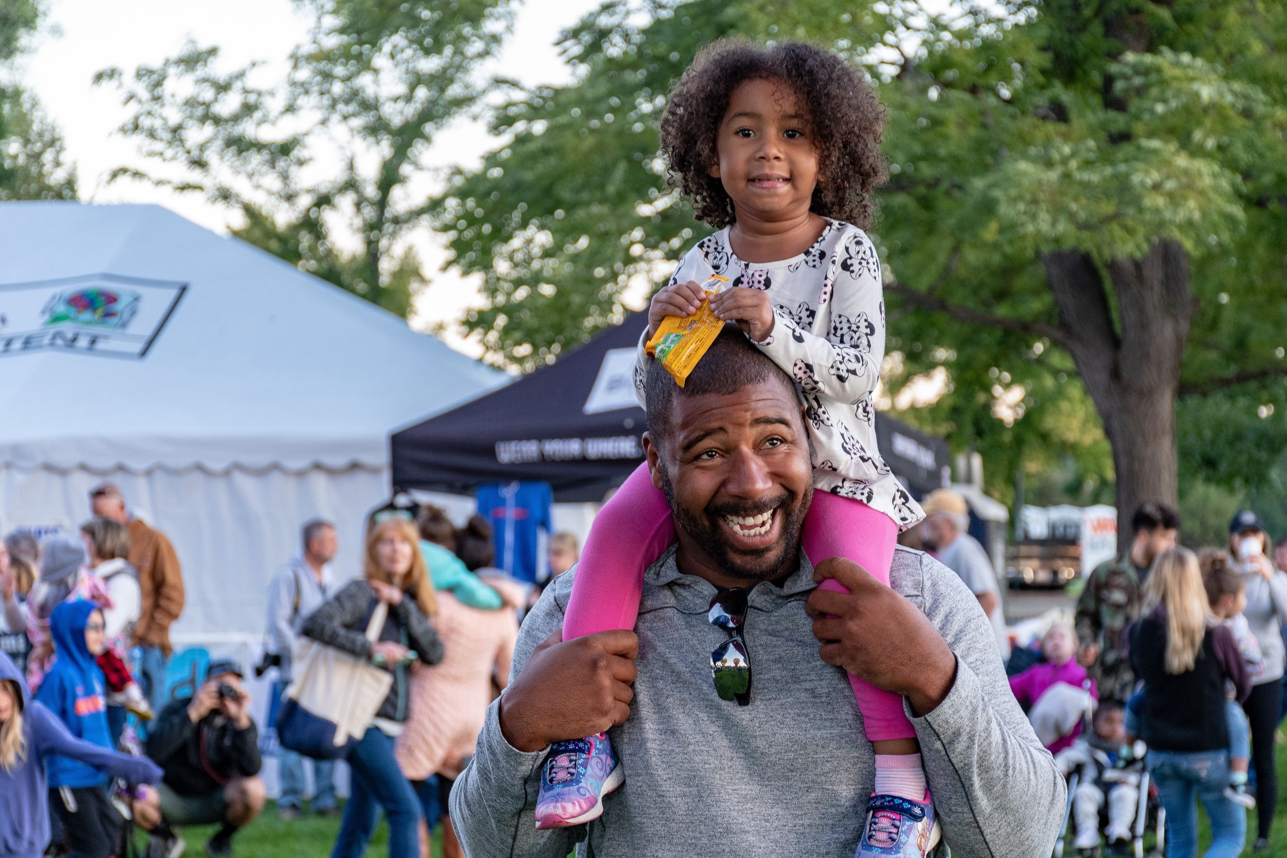 Little girl sits on her father's shoulders at a festival