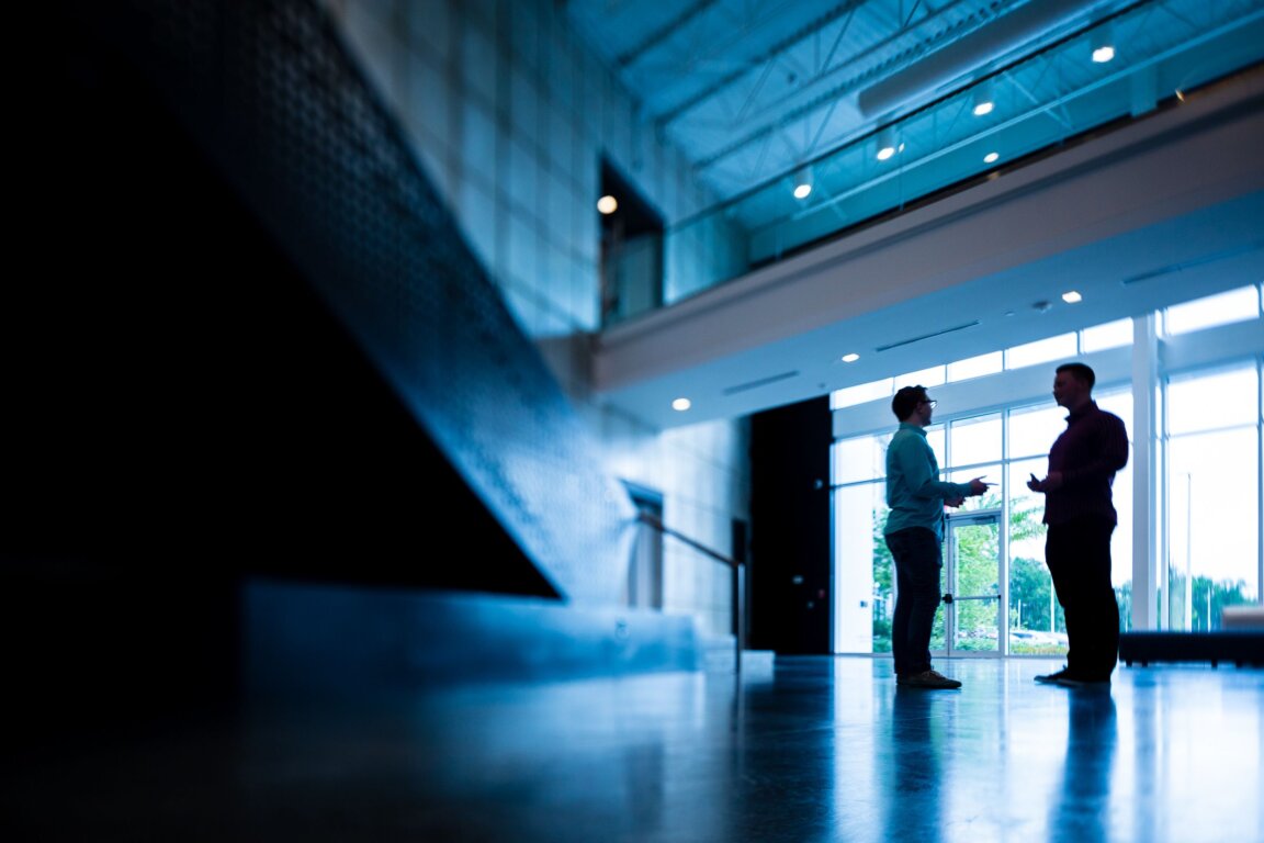 Two men talk in a large blue, modern office lobby