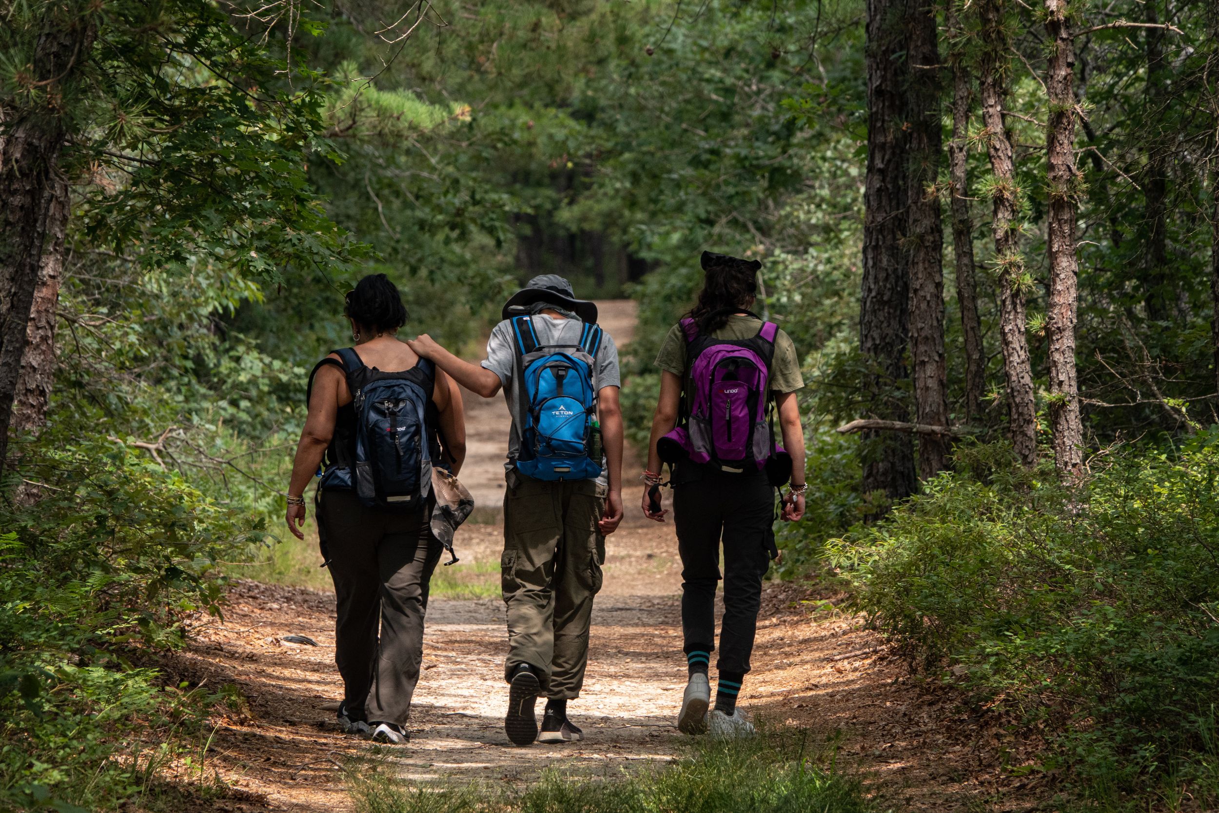 Group of three people walk down hiking trail